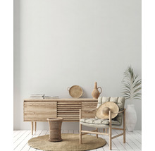 Helles Wohnzimmer mit Holzkommode, Sessel, Strohhut und Dekorationen auf einem runden Teppich.