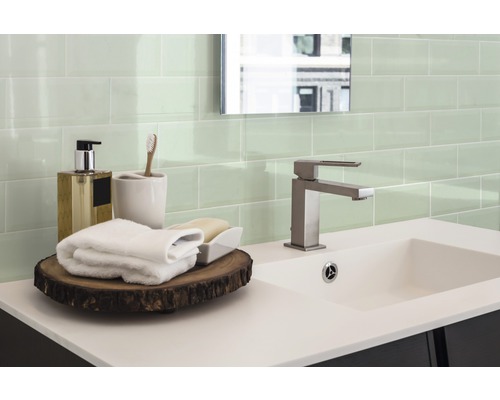 Badezimmer mit Waschbecken, Armatur, Handtüchern und grünen Fliesen