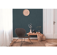 Salon avec fauteuil en rotin, table en bois, vases, tapis en jute et décoration devant un mur vert foncé