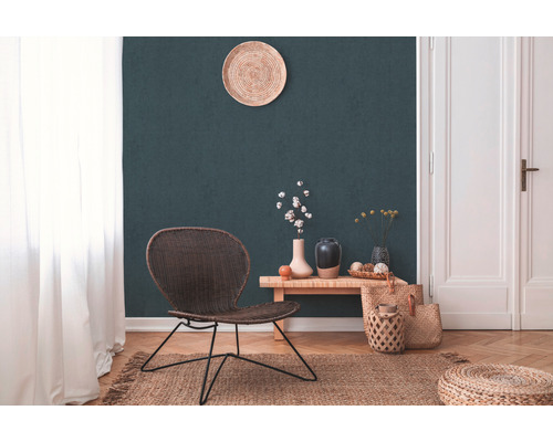 Salon avec fauteuil en rotin, table en bois, vases, tapis en jute et décoration devant un mur vert foncé