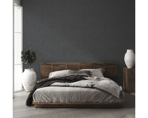 Schlafzimmer mit Bett, Holzkopfteil, Pflanze im Topf und Vase auf einem Holzsockel vor einer strukturierten Wand