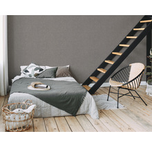 Schlafzimmer mit Bett, Leiter und Korbsessel auf hellem Holzboden vor einer grauen Wand