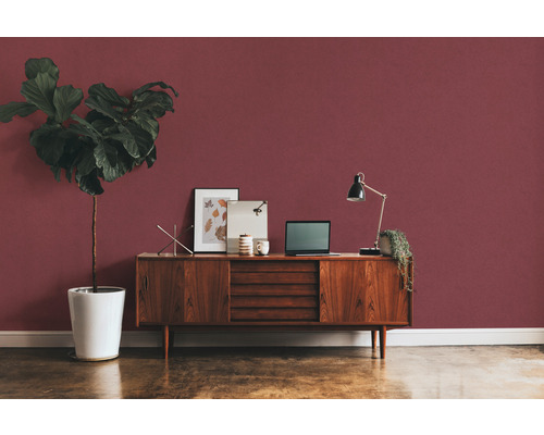 Pièce avec commode, lampe de table, ordinateur portable et plante d''intérieur devant un mur rouge