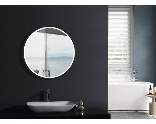 Badezimmer mit rundem Spiegel, Waschbecken, Badewanne und Fenster