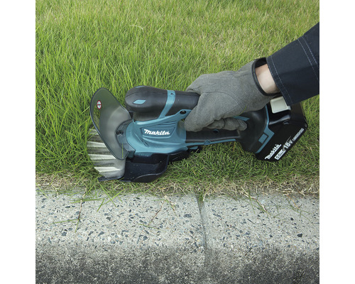 Coupe-bordures Makita en cours d''utilisation pour couper l''herbe le long d''une bordure en béton