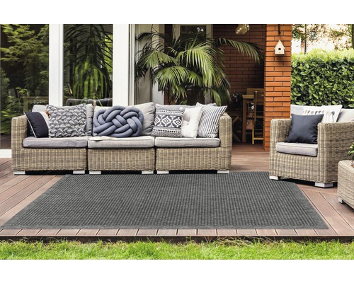 Extérieur avec coin salon en rotin et tapis gris sur une terrasse en bois