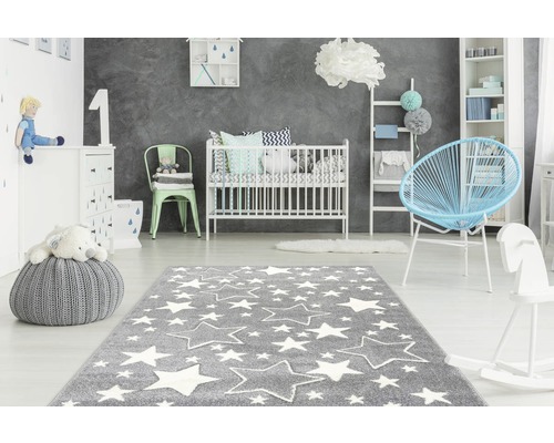 Kinderzimmer mit grauem Teppich und weißen Sternen, Babybett, Kommode und Spielzeug.