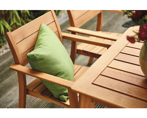 Gartenszene mit Holztisch und Stühlen, einem grünen Kissen und Blumen in einer Vase.