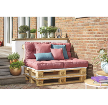 Salon de jardin en palettes Europe avec coussins et oreillers devant un mur en briques