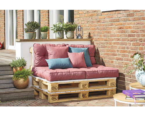 Salon de jardin en palettes Europe avec coussins et oreillers devant un mur en briques