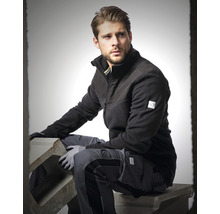 Homme en vêtements de travail avec veste polaire et pantalon de travail assis sur un bloc de béton