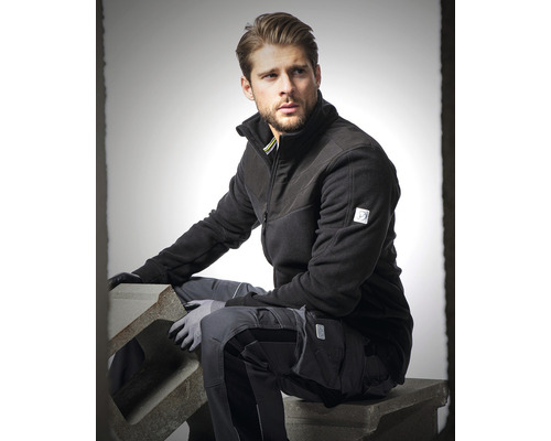Homme en vêtements de travail avec veste polaire et pantalon de travail assis sur un bloc de béton