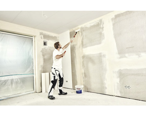 Un homme utilise un rouleau à peinture sur un mur dans une pièce en cours de rénovation.