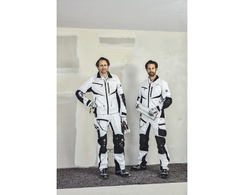 Deux artisans en vêtements de travail devant un mur intérieur.