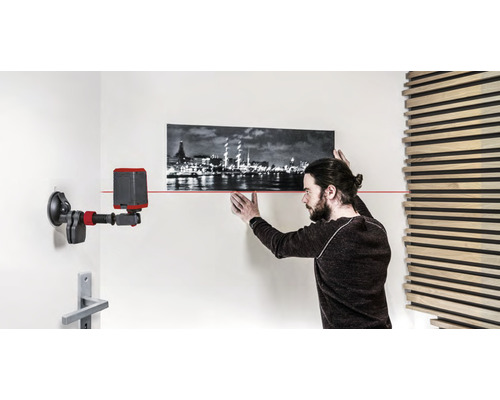Un homme aligne une photo avec un niveau laser sur le mur.