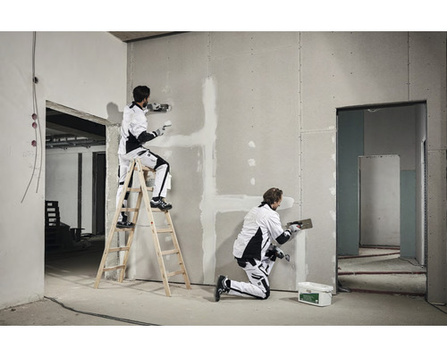 Zwei Handwerker spachteln eine Gipskartonwand in einem Rohbau.