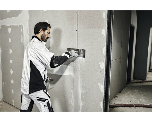 Ein Mann verspachtelt eine Gipskartonwand mit einem Spachtel.