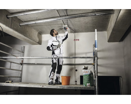 Artisan sur un échafaudage appliquant du plâtre au plafond avec une spatule. Un sac d''enduit est visible à l''arrière-plan.