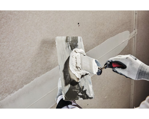 Une personne enduit un mur avec un couteau à mastic.