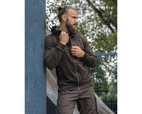 Mann mit Bart und Dutt trägt eine Arbeitsjacke mit Kapuze und Arbeitshose