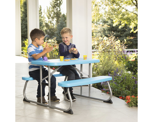 Zwei Kinder sitzen an einem Picknicktisch mit Bänken im Freien und spielen.