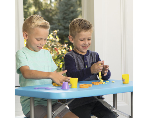 Zwei Kinder spielen mit Spielzeugknete an einem blauen Tisch.