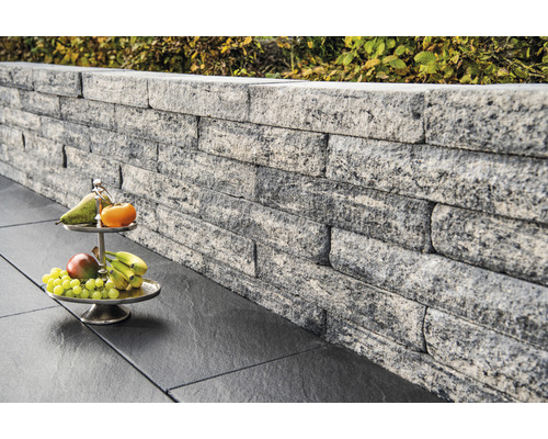 Mur en pierre grise empilée avec une corbeille de fruits sur des carreaux de sol foncés