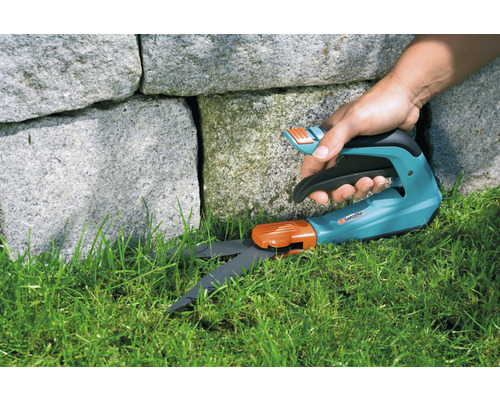 Gartenschere schneidet Rasen an einer Steinmauer