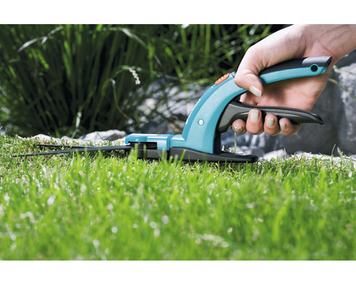 Eine Hand hält eine Grasschere über einen Rasen.