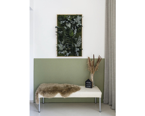 Dekoratives Moosbild mit verschiedenen Pflanzenarten, darunter Farne und Eukalyptus, an einer Wand über einer Bank mit Schaffell