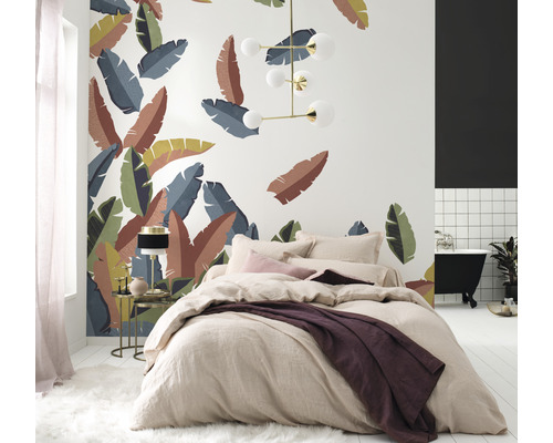 Schlafzimmer mit Bett vor einer Wand mit tropischen Blättern, einer Lampe und einem Badezimmer mit Badewanne.