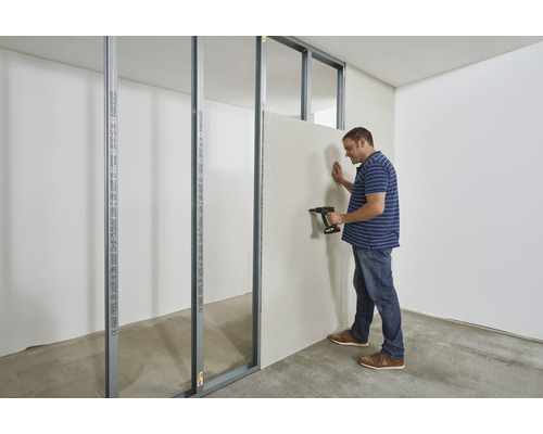 Mann befestigt Trockenbauwand mit Bohrmaschine an Metallprofilen im Rohbau