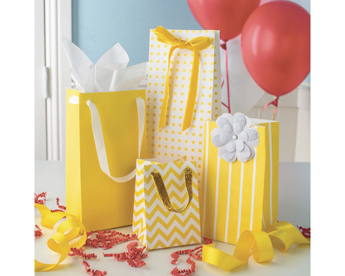 Gelbe Geschenktüten mit verschiedenen Mustern, darunter Punkte, Streifen und Zickzackmuster, mit dekorativen Elementen wie Schleifen und einer Blume