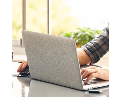 Eine Person arbeitet an einem Laptop mit einer Maus und einem USB-Stick auf einem Tisch.
