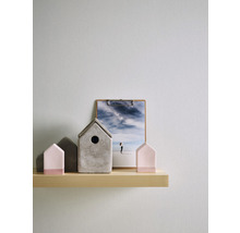 Dekorative Häuser aus Beton und Holz auf einem Regal, mit einer Fotografie im Hintergrund.