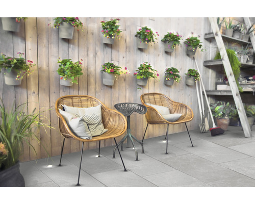 Terrassenszene mit Rattan-Stühlen, kleinem Beistelltisch und Wanddekoration mit Blumentöpfen.