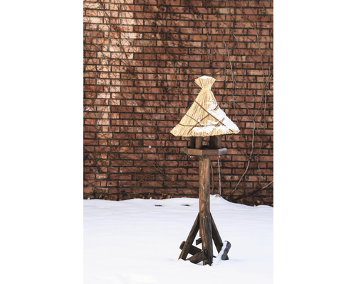 Maison pour oiseaux en bois avec toit de chaume dans un jardin enneigé