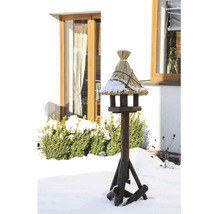 Mangeoire à oiseaux avec toit de chaume sur un support en bois dans un jardin enneigé.
