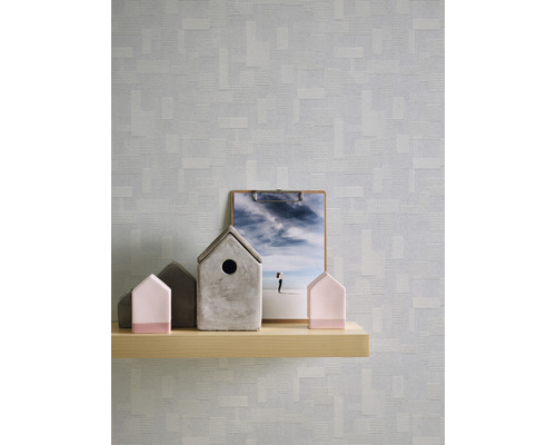 Scène avec une étagère en bois sur laquelle sont posées des maisons décoratives et un presse-papier devant un papier peint à motifs.