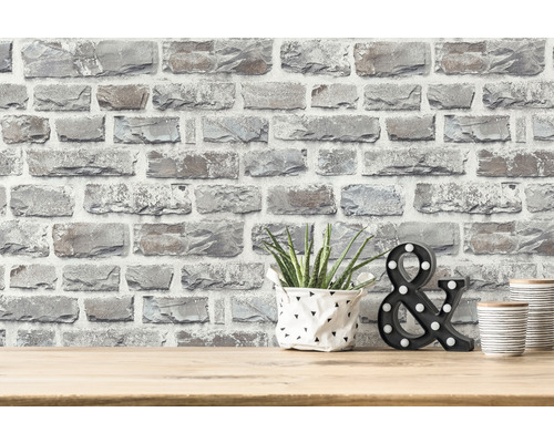 Dekorative Steinoptik Tapete an einer Wand mit Pflanze, dekorativem &-Zeichen und dekorativen Dosen auf einem Tisch