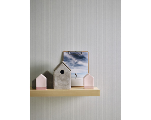 Scène décorative avec des figurines de maison, une pince et une étagère en bois devant un papier peint.