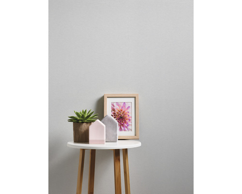 Gros plan d'une table d'appoint avec une plante d'intérieur, des maisons décoratives et un cadre photo devant un papier peint structuré.