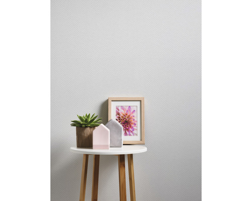 Une pièce lumineuse avec un papier peint texturé, une table ronde avec des décorations : une plante, deux figurines de maison et une photo de fleur encadrée.