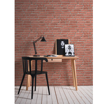 Schreibtisch mit Stuhl, Lampe und Wandbildern vor einer Backsteinmauer