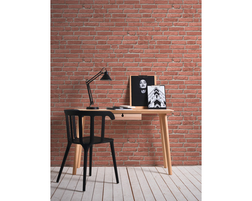 Schreibtisch mit Stuhl, Lampe und Wandbildern vor einer Backsteinmauer