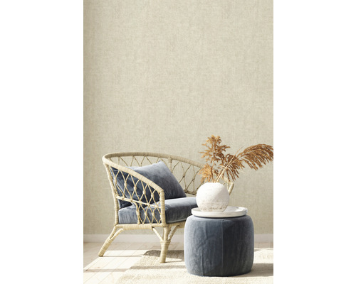 Dekorative Inneneinrichtung mit Rattansessel, Kissen und Beistelltisch vor einer beigen Tapete.