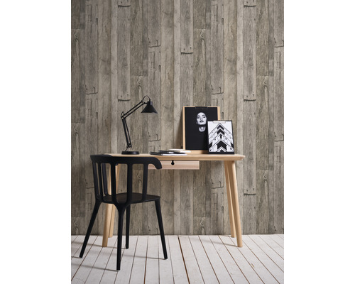 Arbeitszimmer mit Schreibtisch, Stuhl, Schreibtischlampe und Dekoration vor einer Tapete in Holzoptik