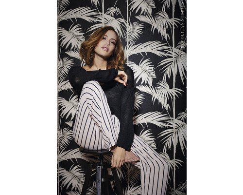 Frau sitzt vor einer dunklen Tapete mit Pflanzenmotiven