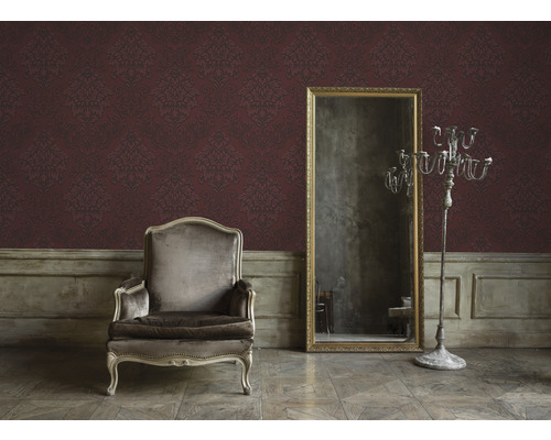 Intérieur avec fauteuil, miroir et papier peint ornemental pour une ambiance chaleureuse.