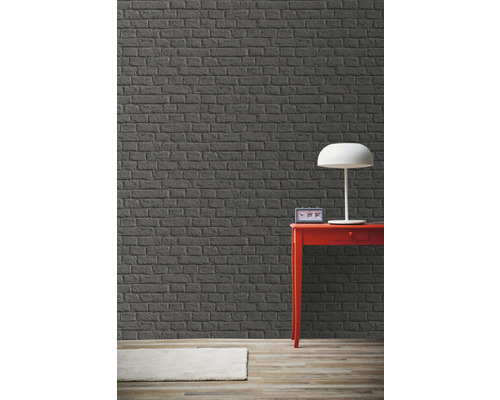 Zimmer mit grauer Backsteinwand, rotem Tisch und Lampe.